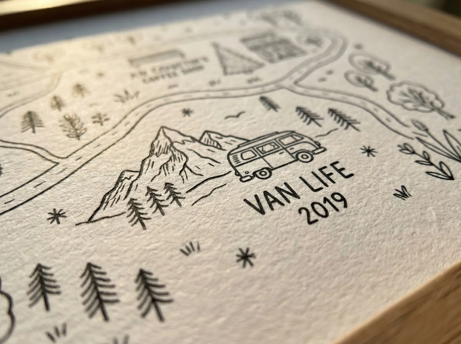 Close-up macro photograph showing the paper grain and ink detail of a printed custom love map. The illustration features a sketched camper van beside mountains with the text Van Life 2019.